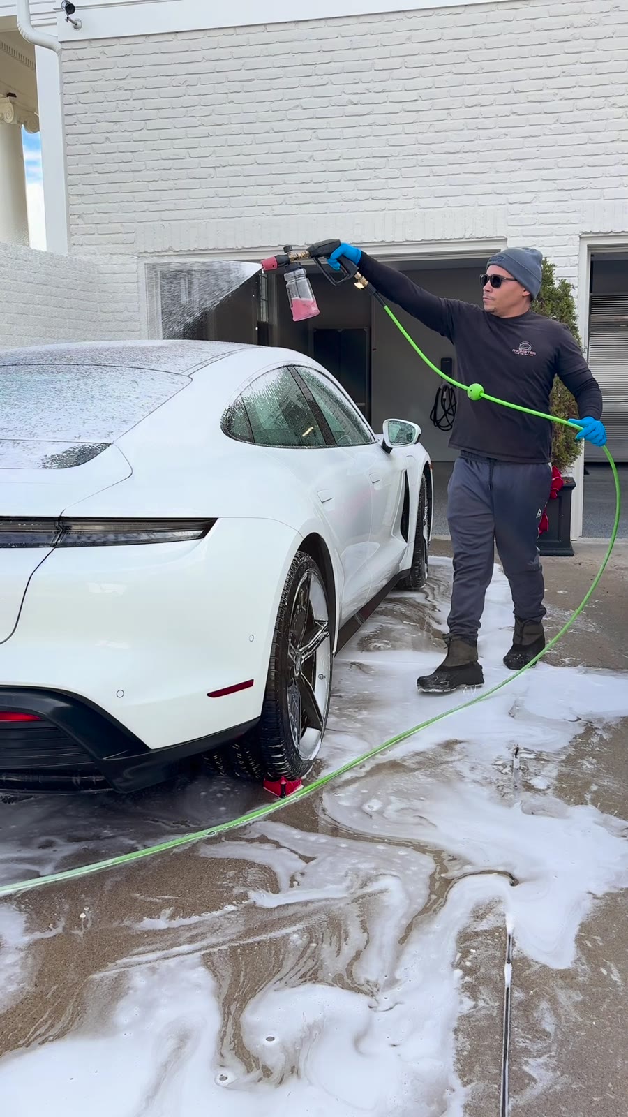 Detailer rinsing thick foam off a Porsche Taycan in a driveway