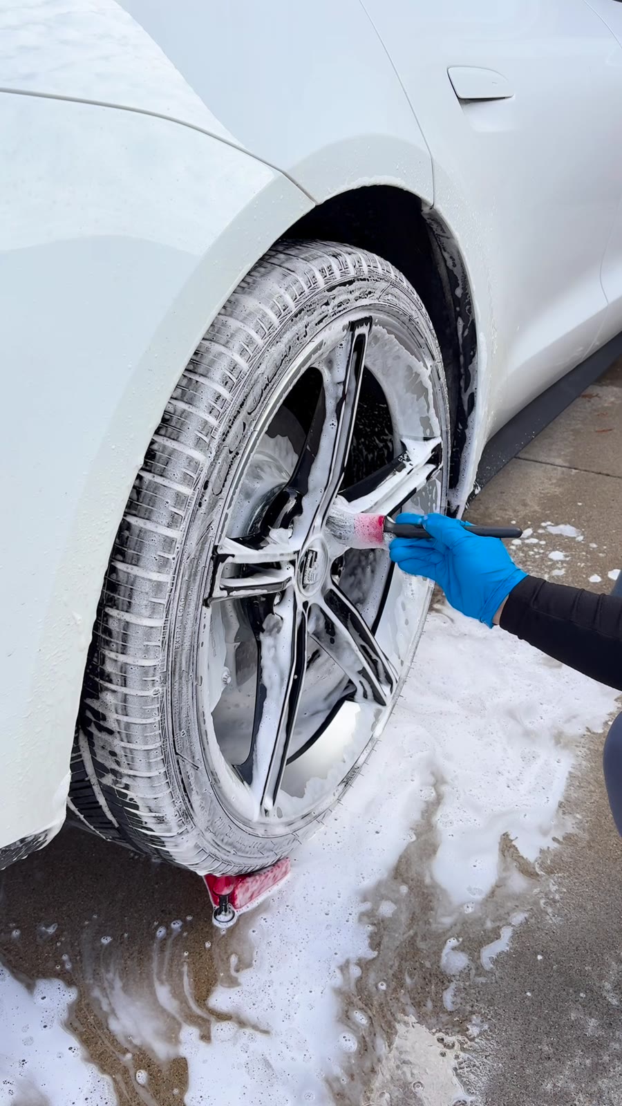 Detailer scrubbing a wheel and tire during a foam wash