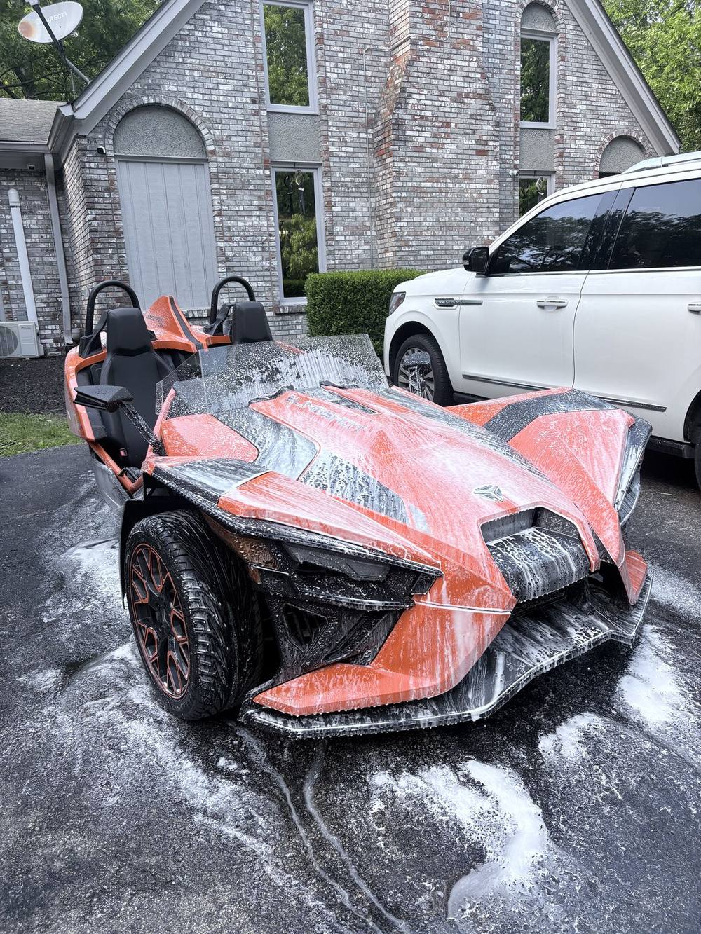 Orange Polaris Slingshot covered in foam during a mobile wash